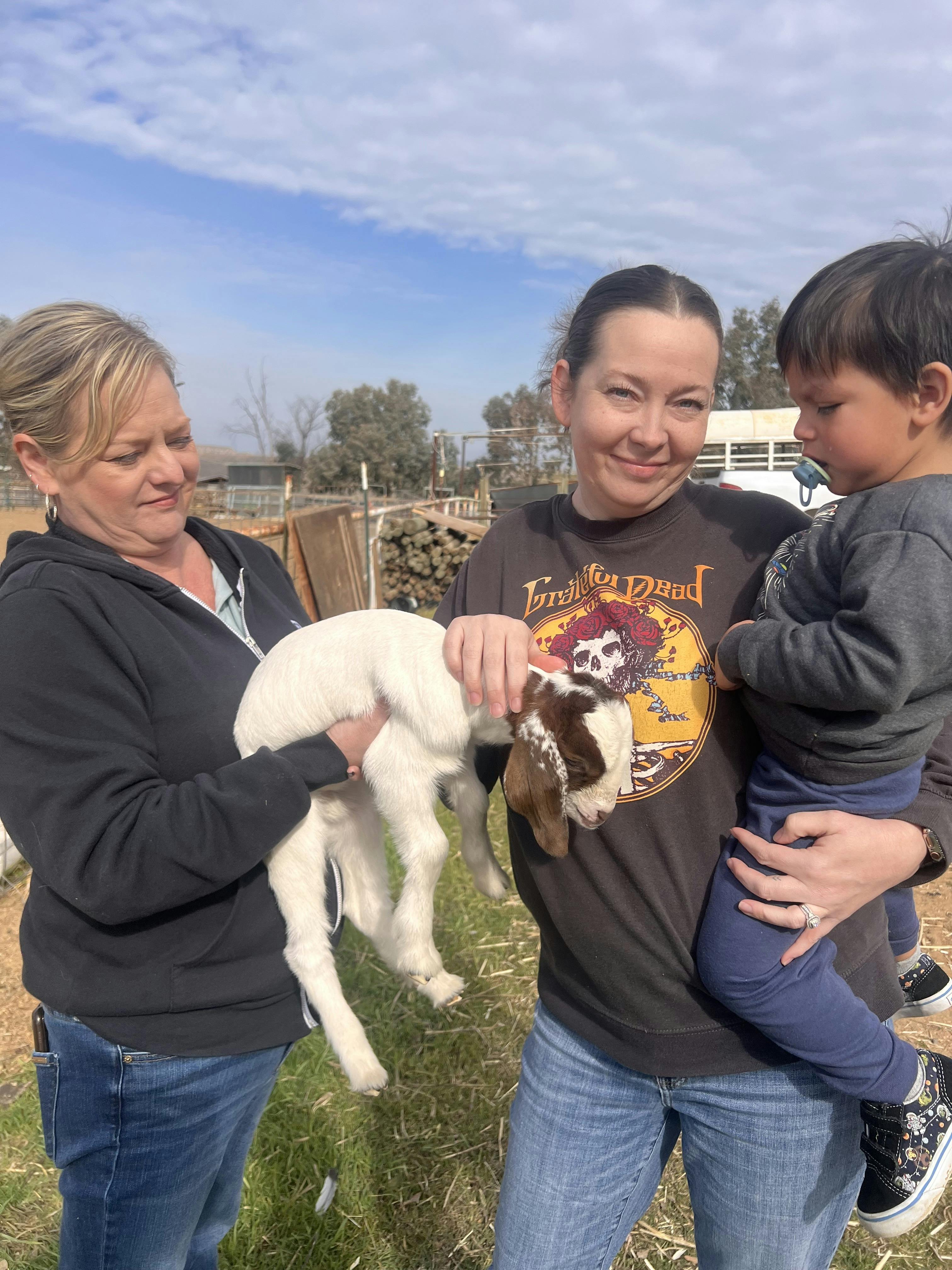 Two people holding a lamb and a child outdoors