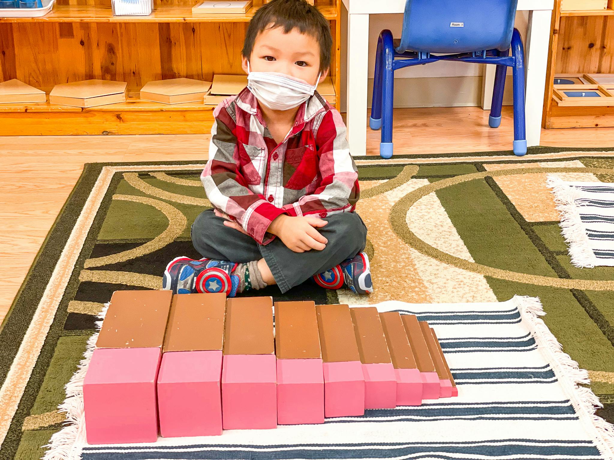 Child in mask sitting on rug with blocks in a classroom