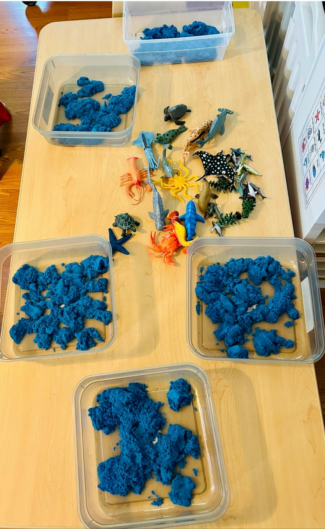 Blue kinetic sand in clear containers with plastic sea animal toys on a table