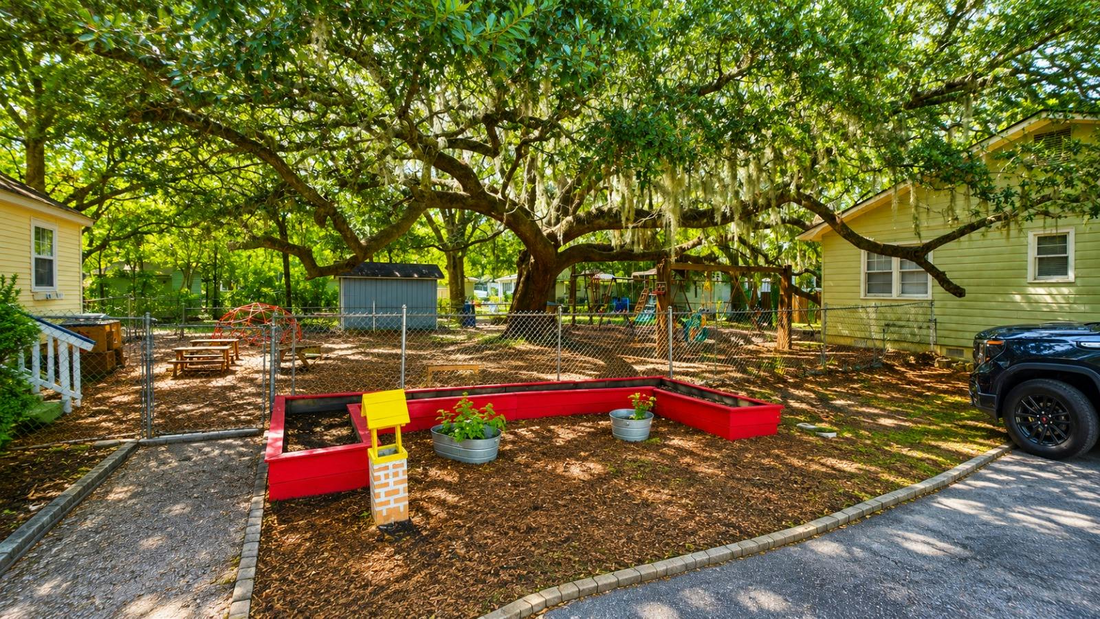 Red raised garden bed with metal planters under a large oak tree