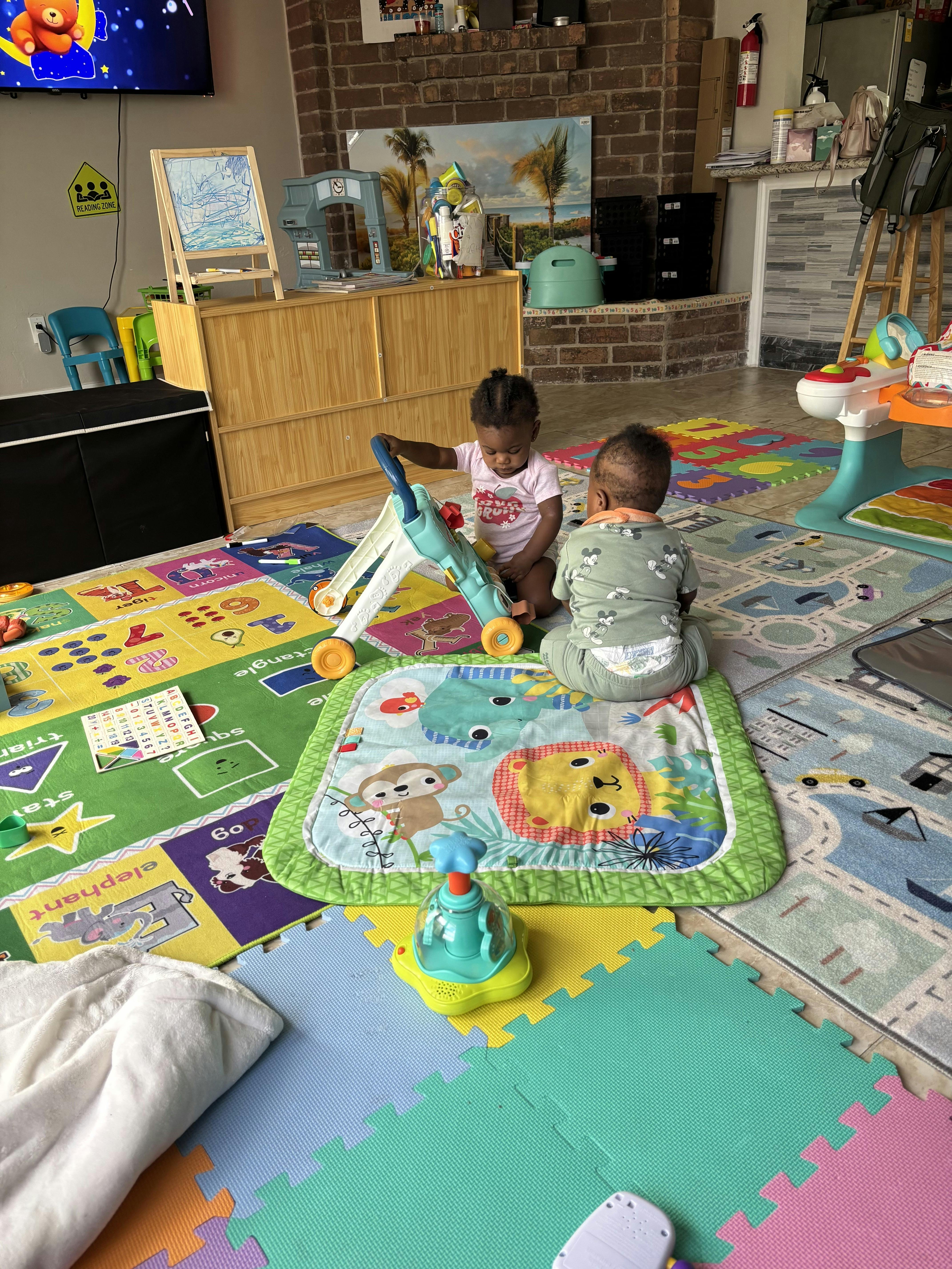 two children playing on a colorful mat, one pushing a walker