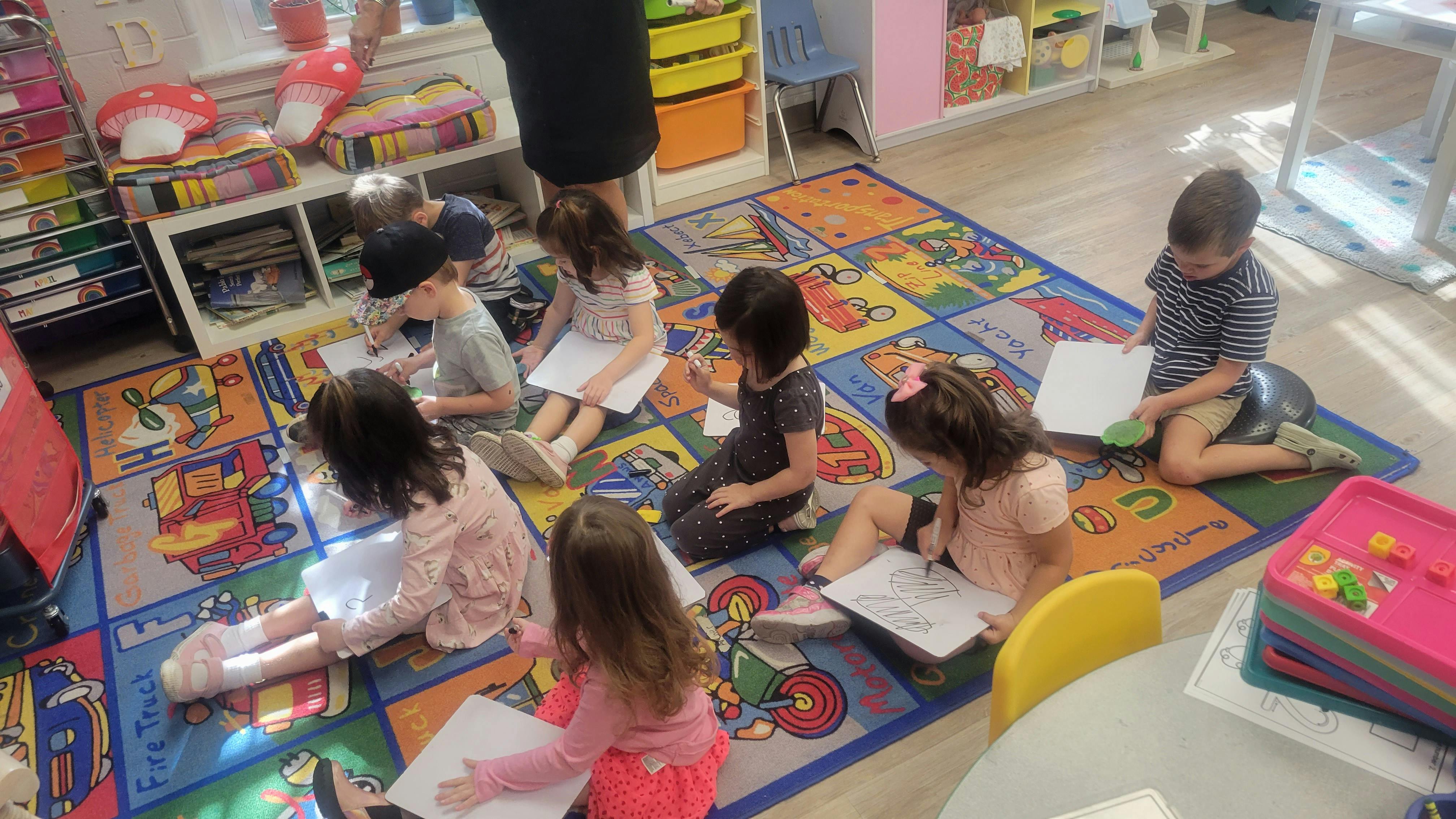 Children sitting on a rug and writing on the floor, writing on paper