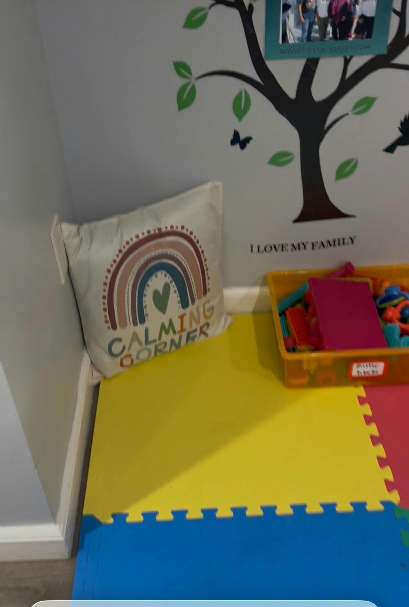 Pillow with rainbow and 'CALMING CORNER' text on a puzzle mat floor next to toys