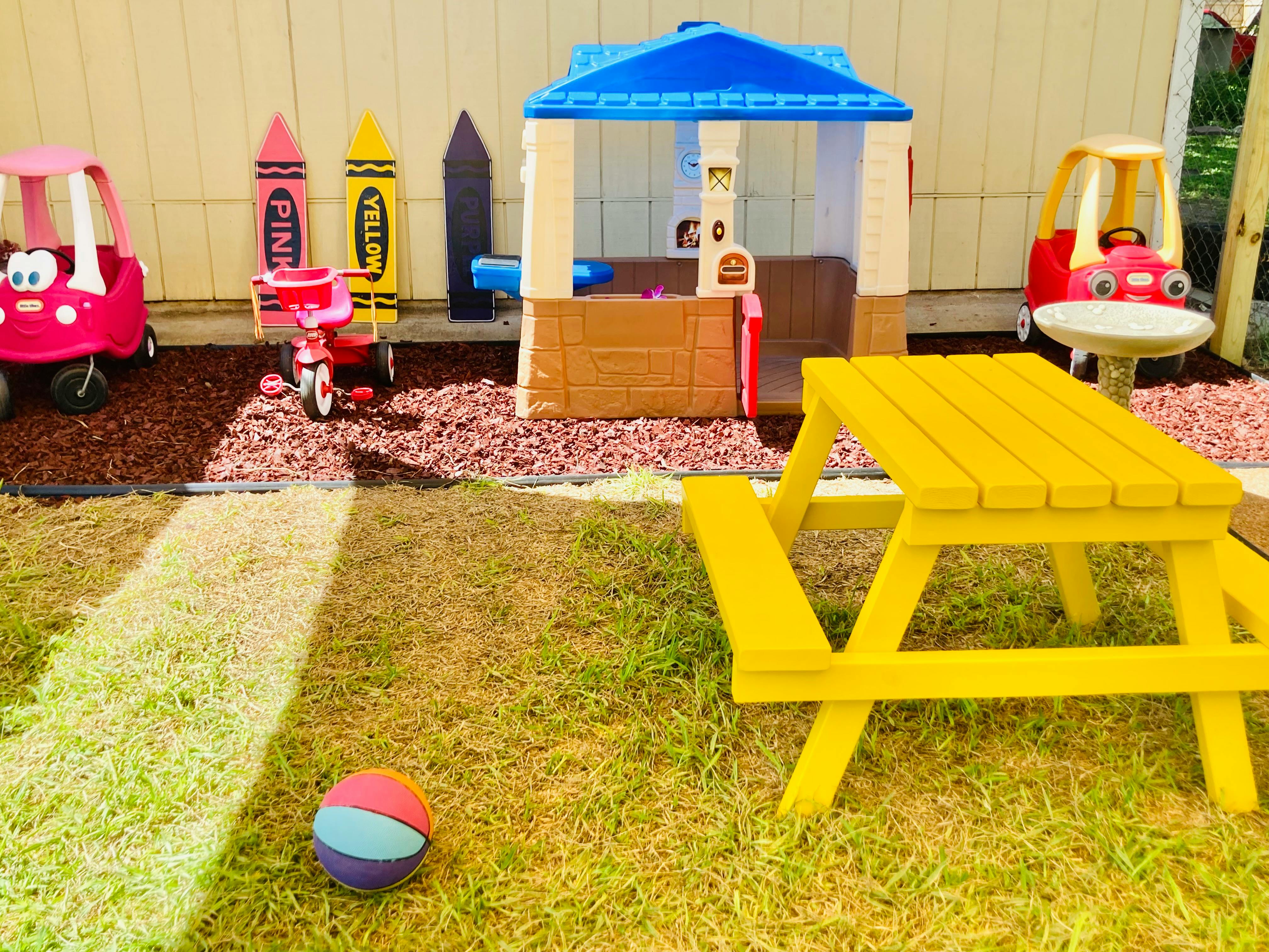 Play area with toy cars, playhouse, and yellow picnic table