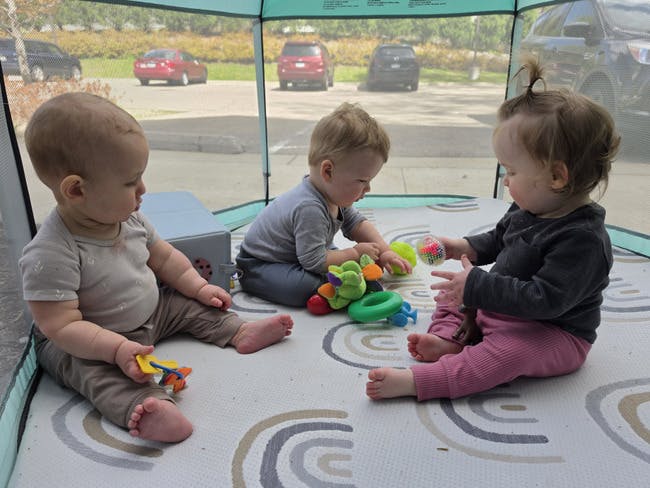 Three children playing with toys on a mat inside a tent