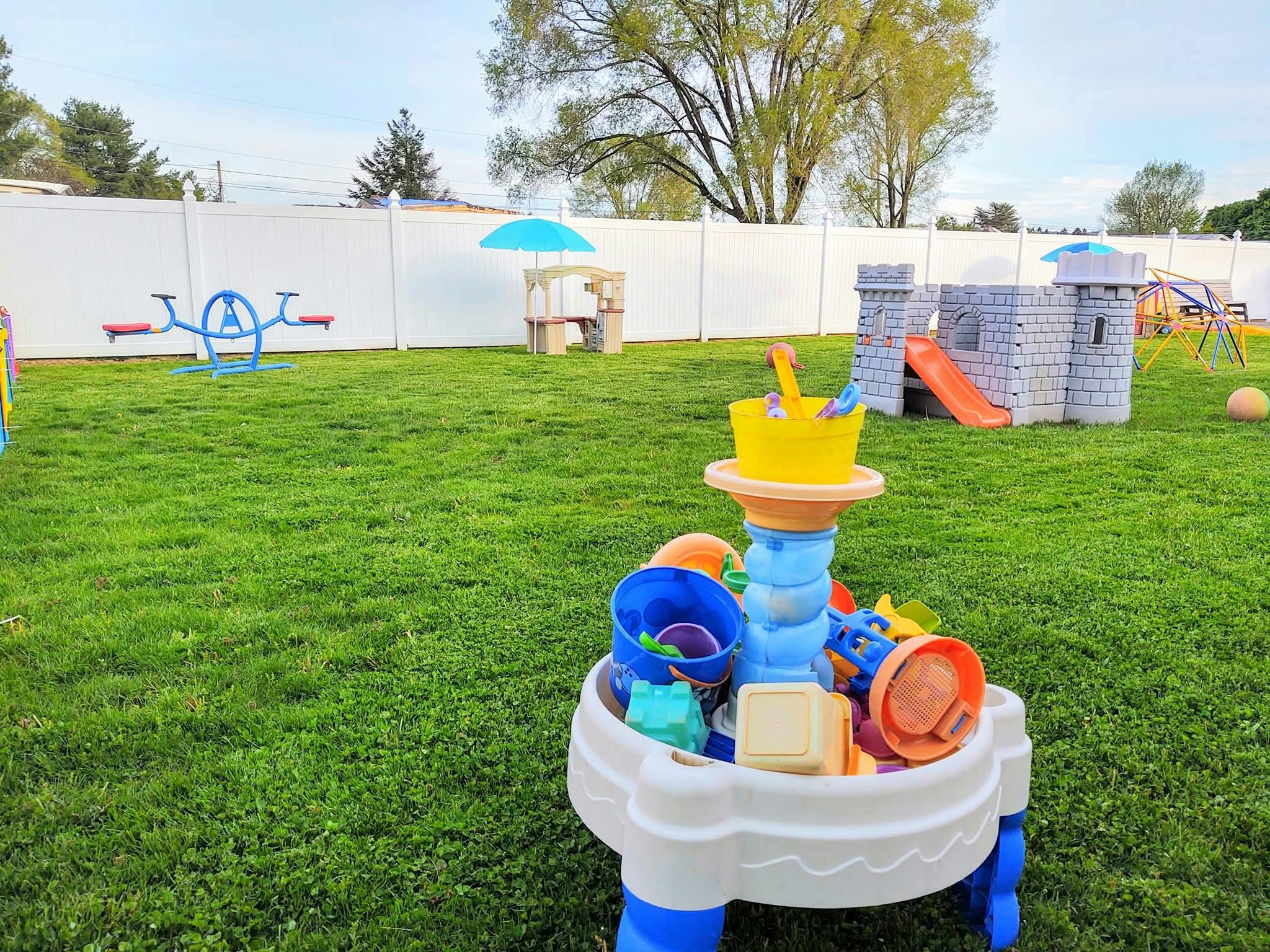 A backyard with a water table filled with toys, a seesaw, and a play castle