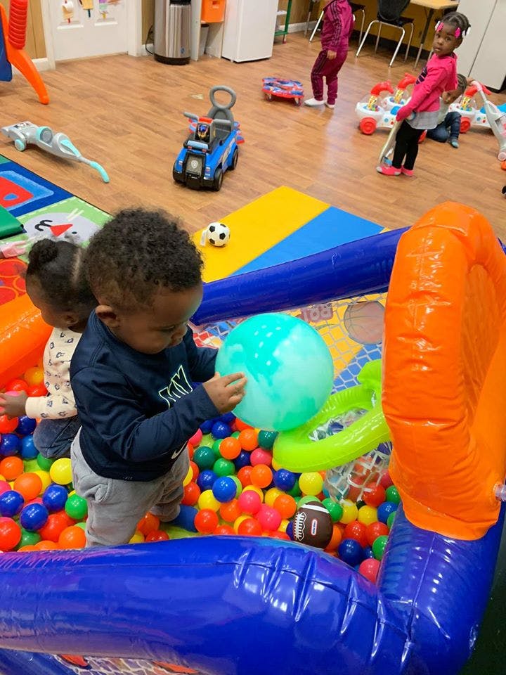 Child holding a large ball in a ball pit with another child nearby