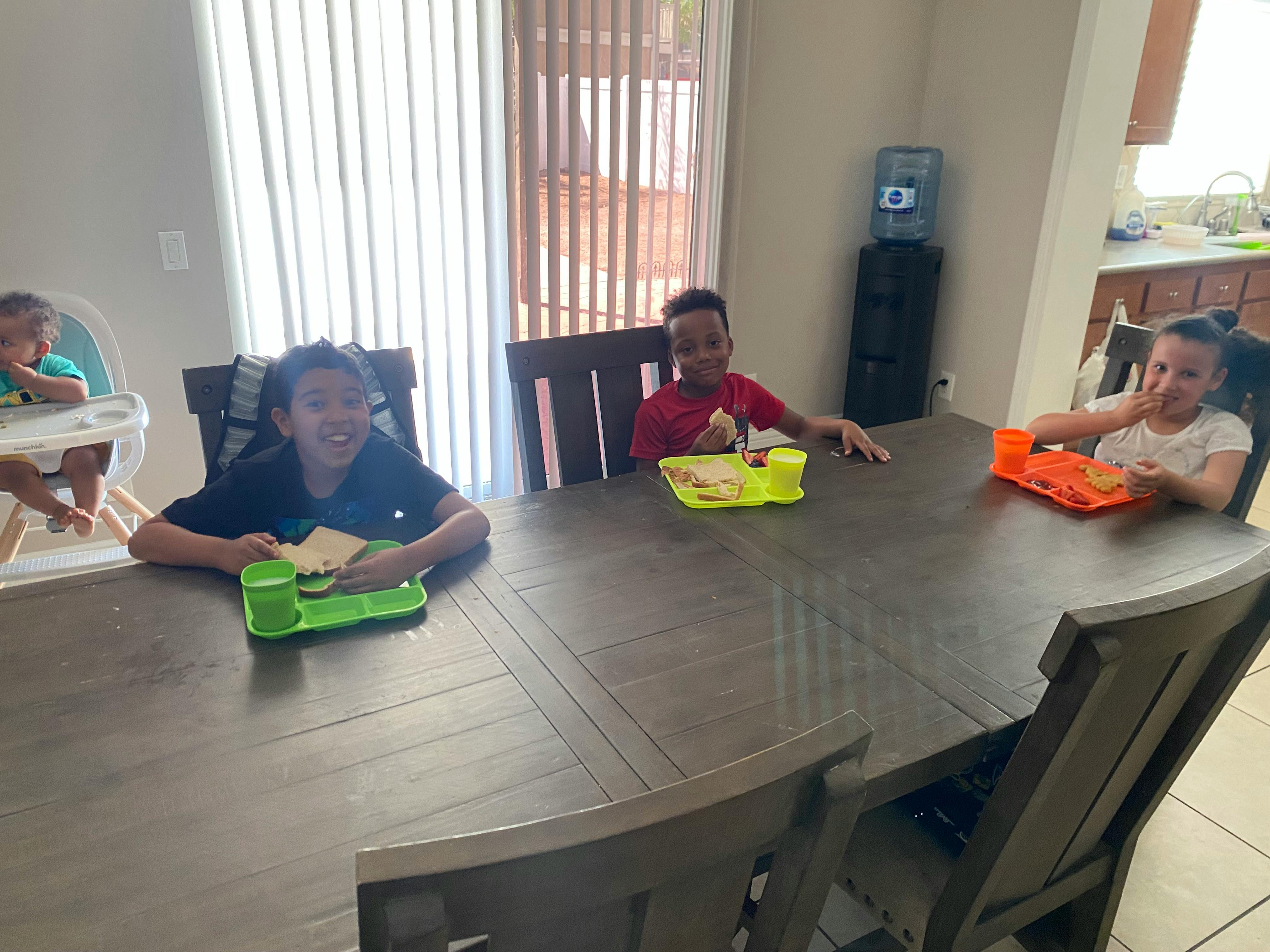 Three children and one teen sitting at a table with plates of food