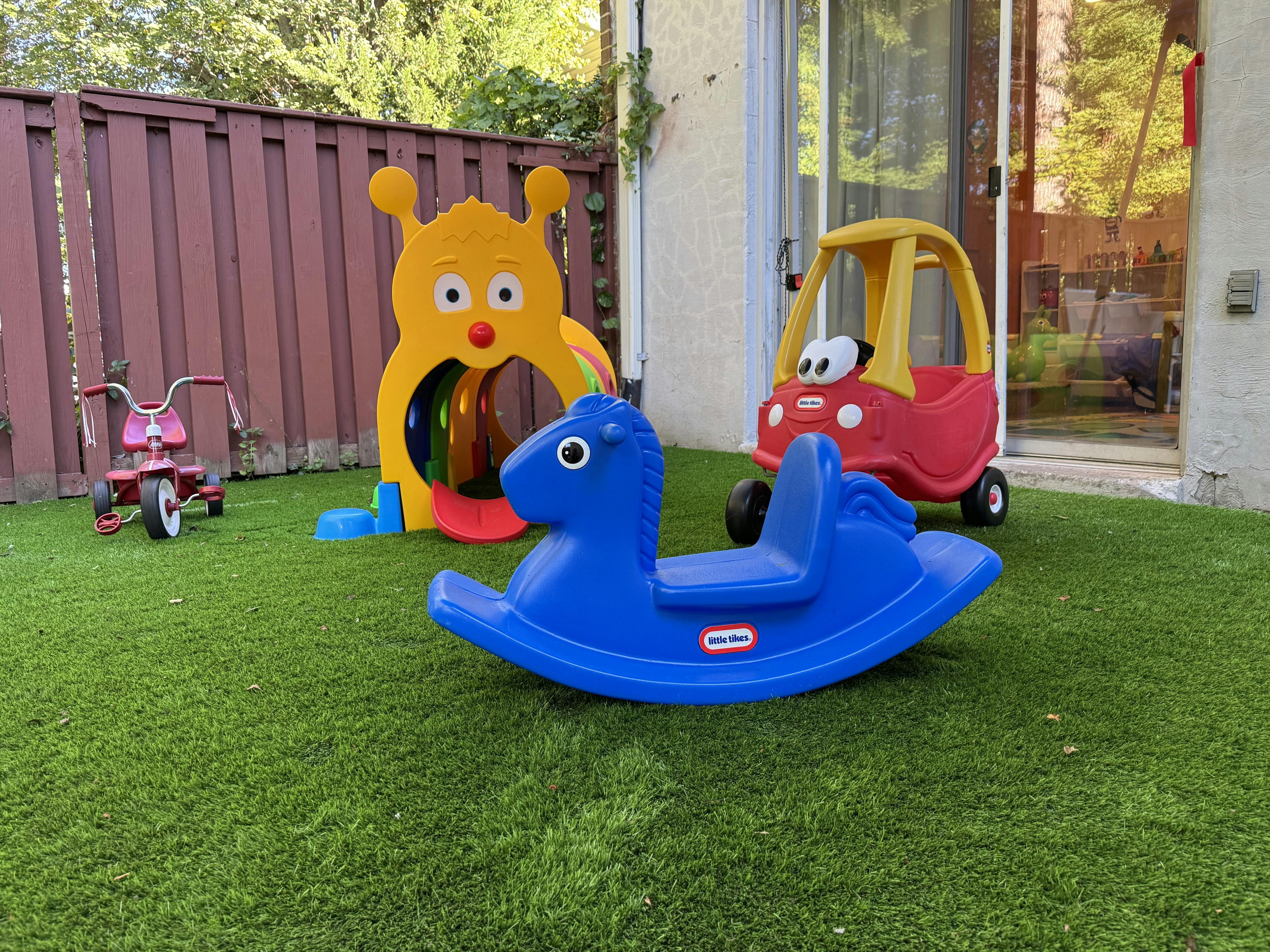 Blue rocking horse, red toy car, and tricycle on green grass