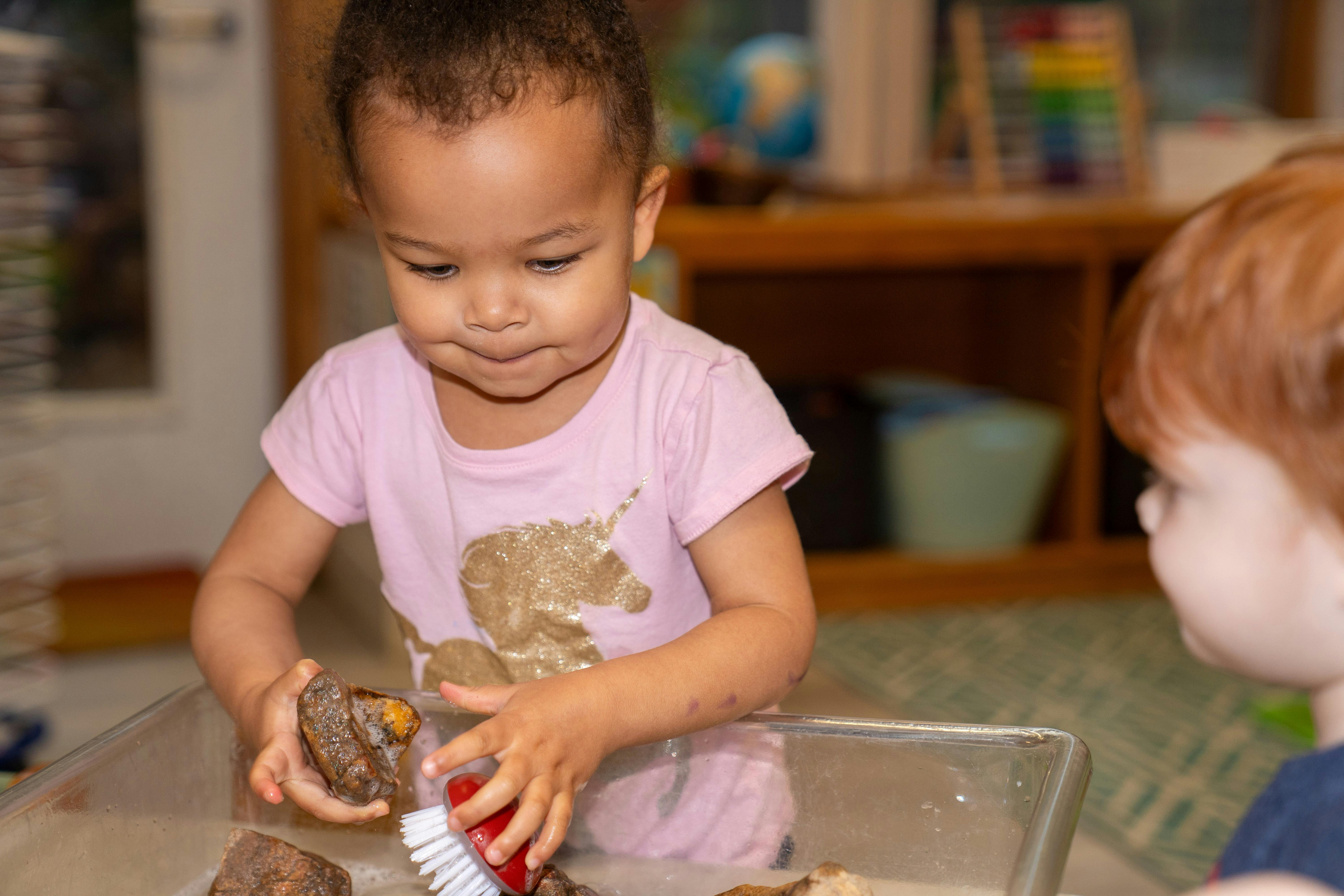 Child cleaning rocks with a brush in a clear bin