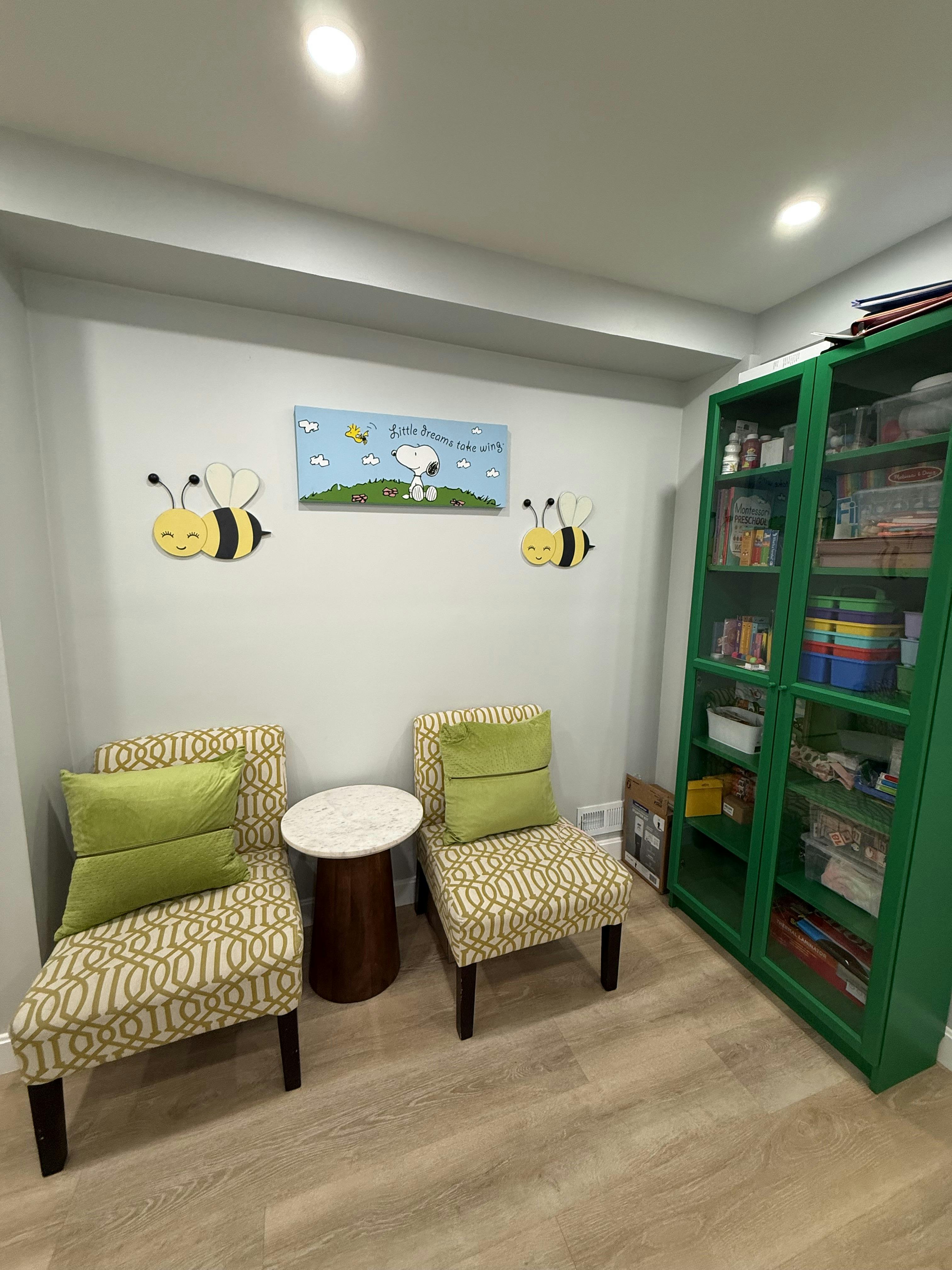 Two armchairs with a small table and a green storage cabinet in a playroom