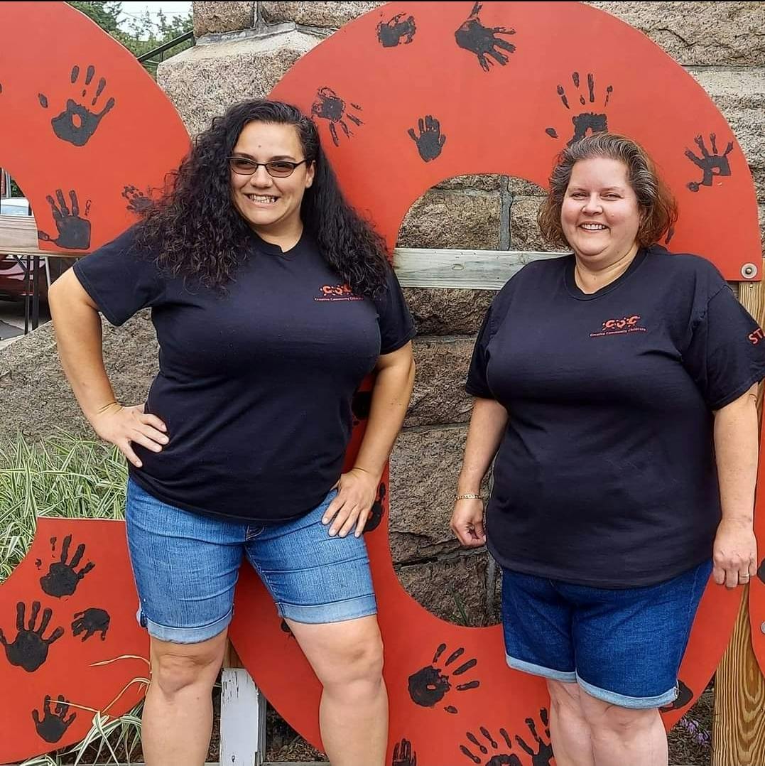 Two people standing in front of a red sign with handprints