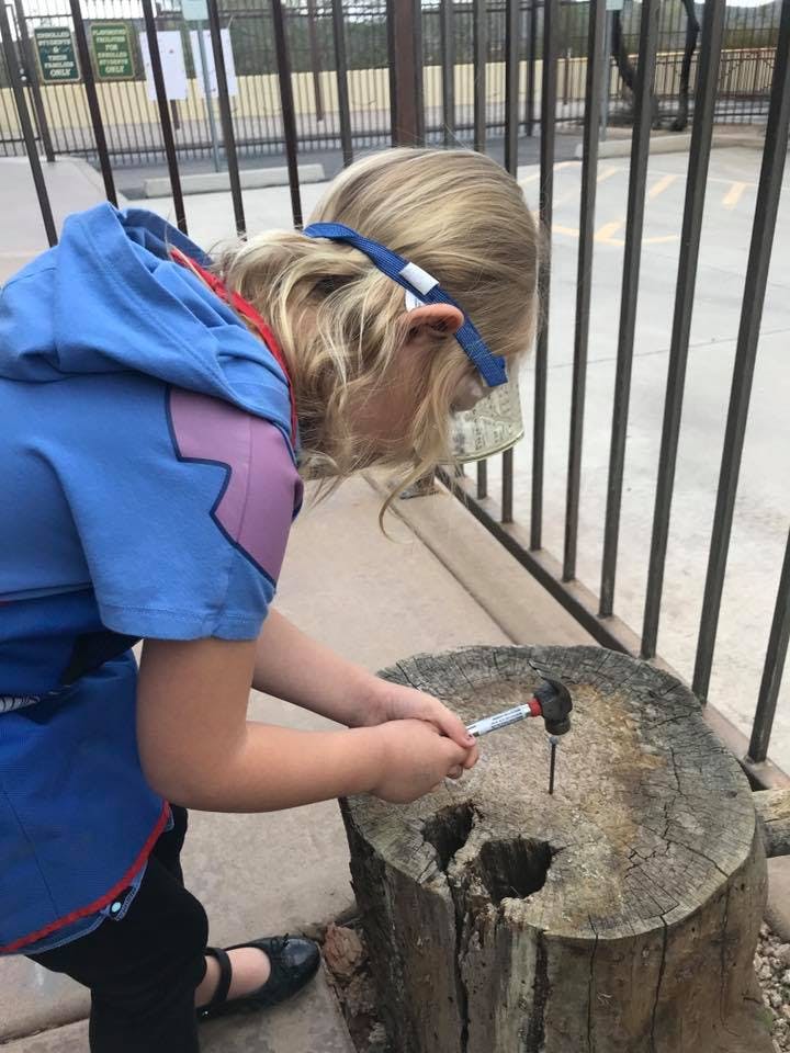 Child wearing safety glasses hammering a nail into a tree stump