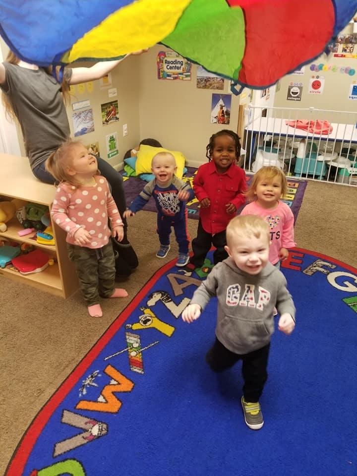 Adult holding a colorful parachute over a group of children in a classroom