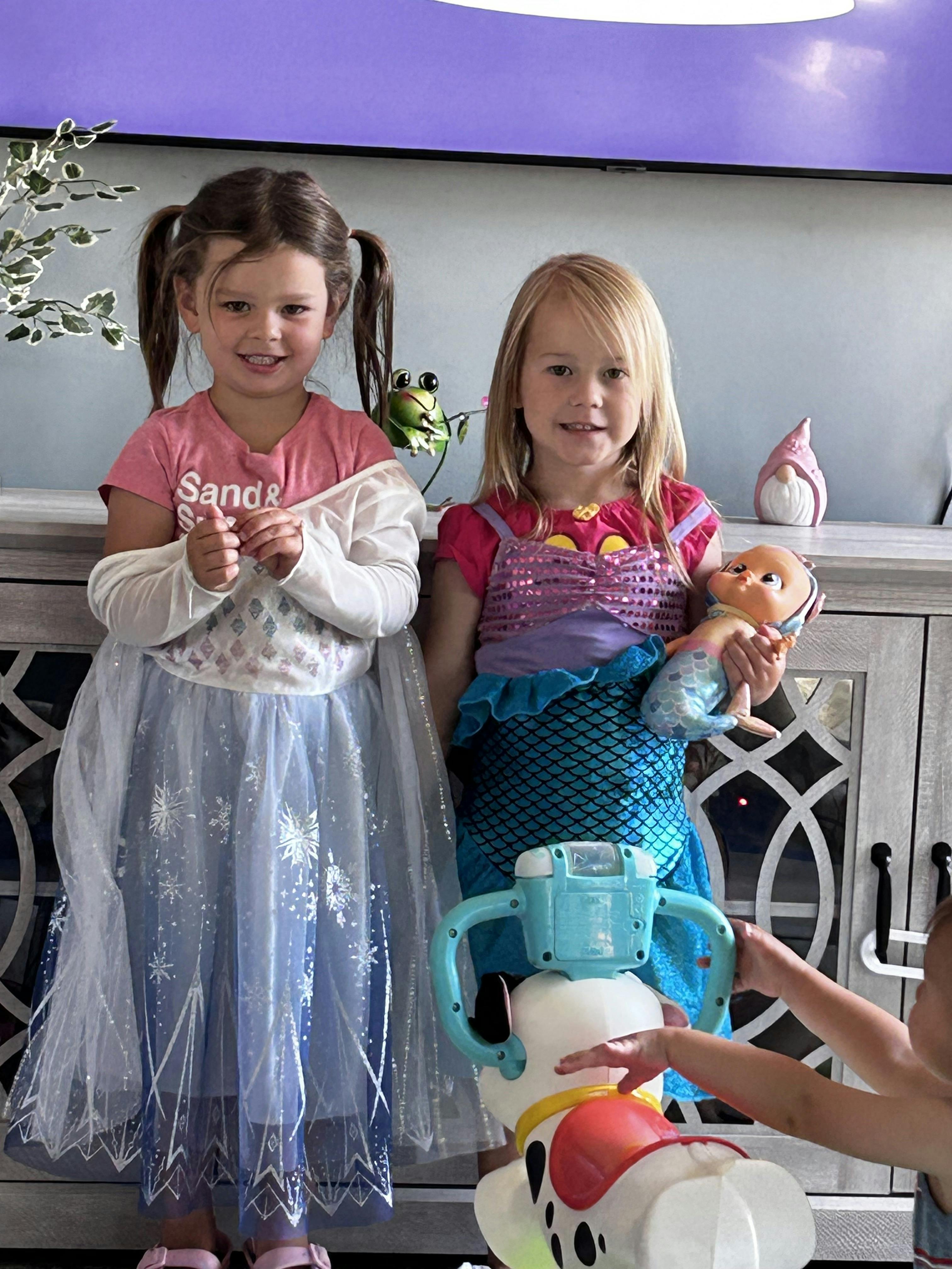 Two young children in costumes, one in a princess dress and one in a mermaid costume