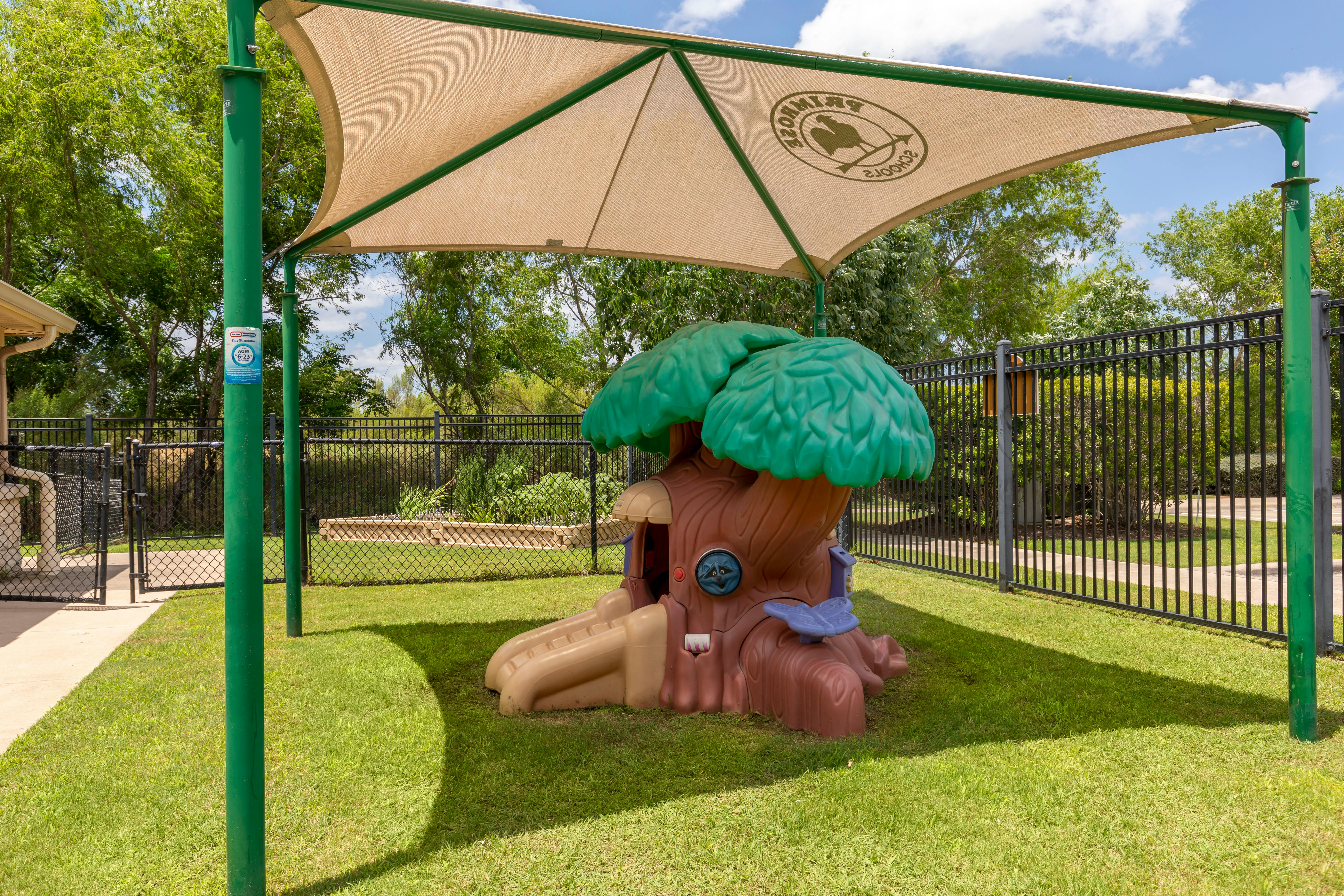 Playground with a treehouse slide and a sunshade with a Primrose Schools logo