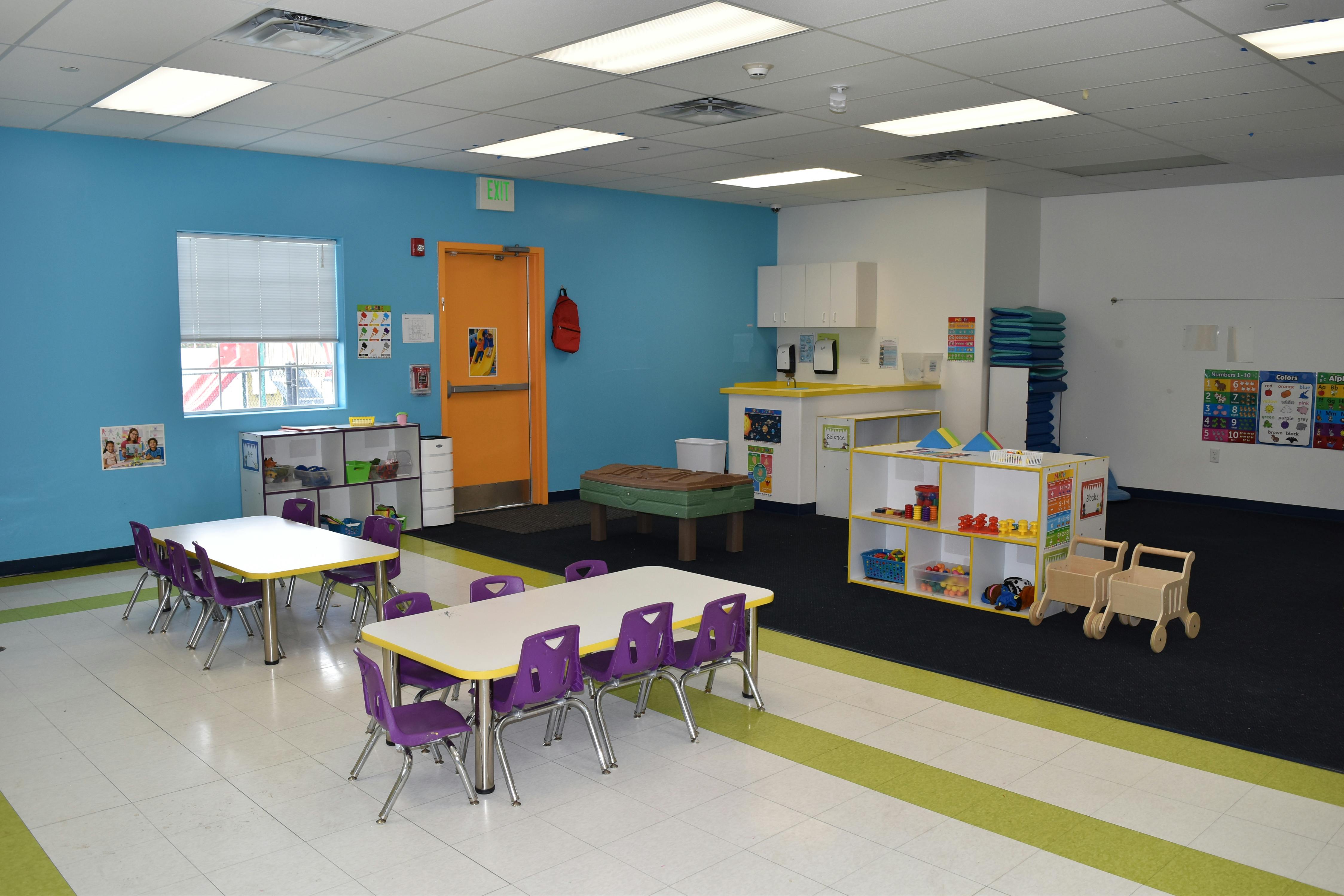 Classroom with small tables and chairs, play kitchen, and toy shelves
