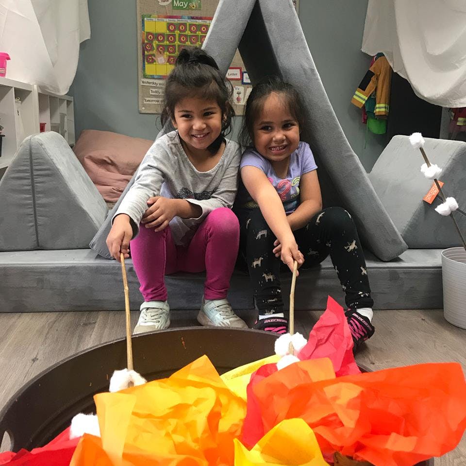 Two children holding sticks with marshmallows over a pretend campfire