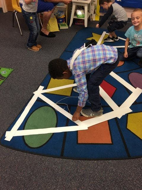 Child bending over to place tape on a colorful rug with shapes