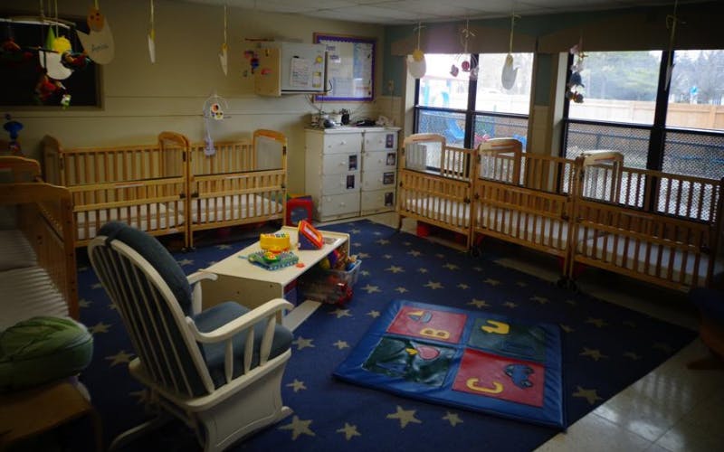 Classroom with multiple cribs, a rocking chair, and play mats on a star-patterned rug