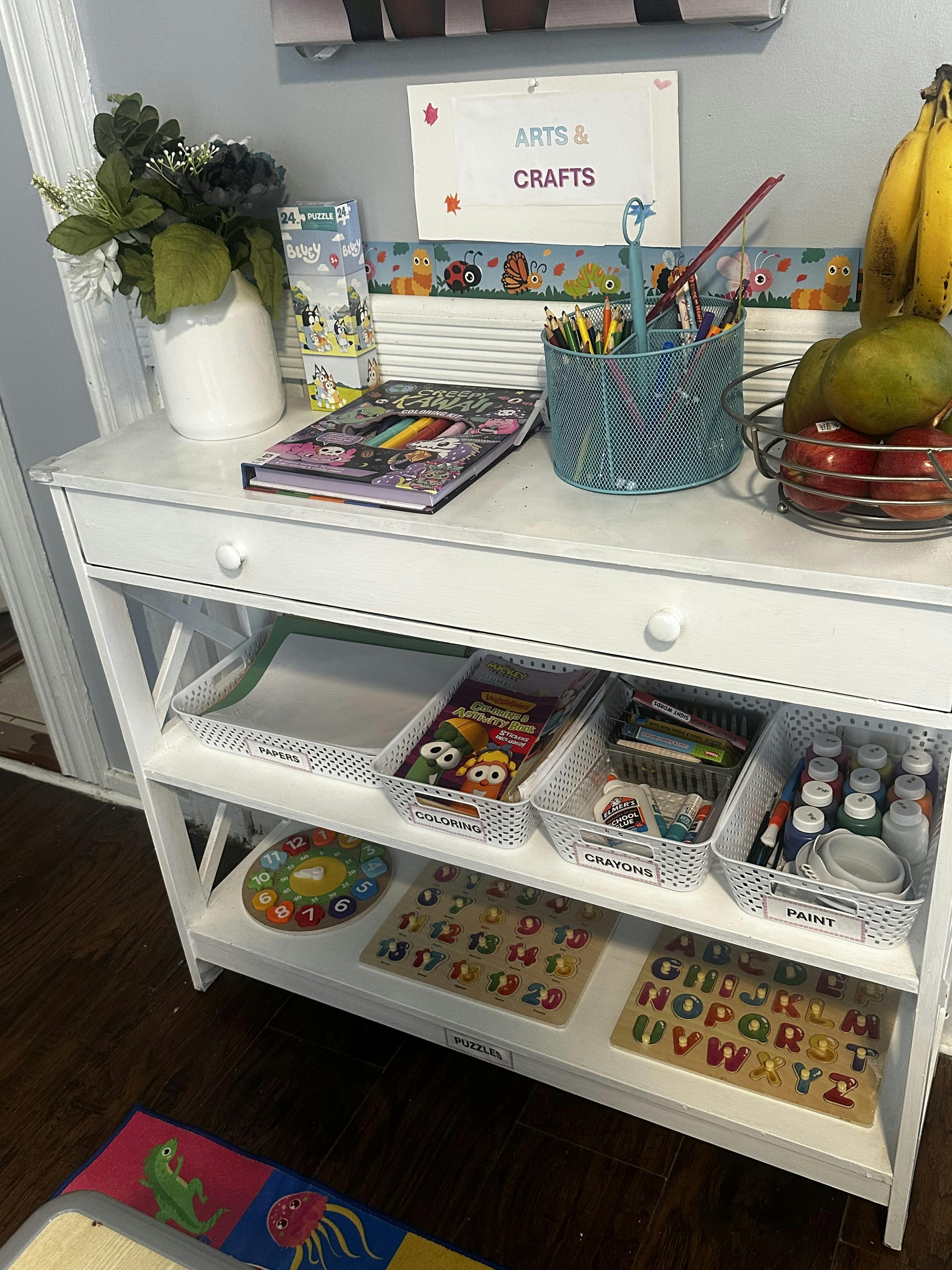 White storage shelf with arts and crafts supplies, puzzles, and fruits