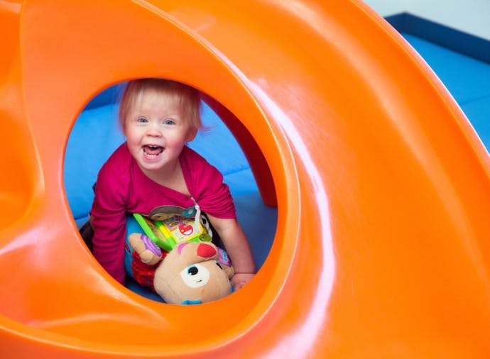 Child in a red shirt playing inside an orange tunnel slide