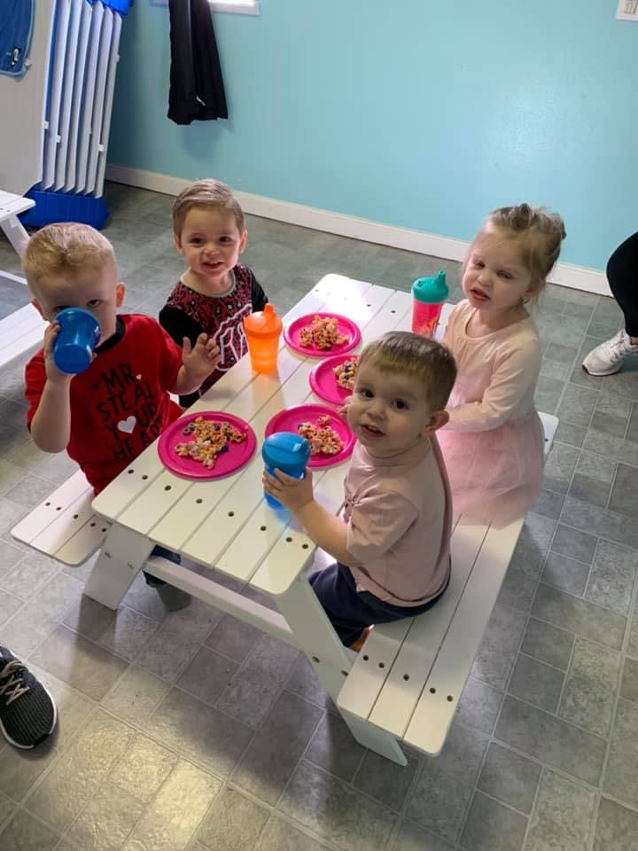 Four children sitting at a small picnic table with plates of food