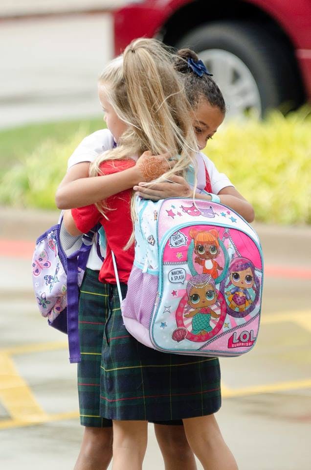 Two children wearing backpacks hugging each other