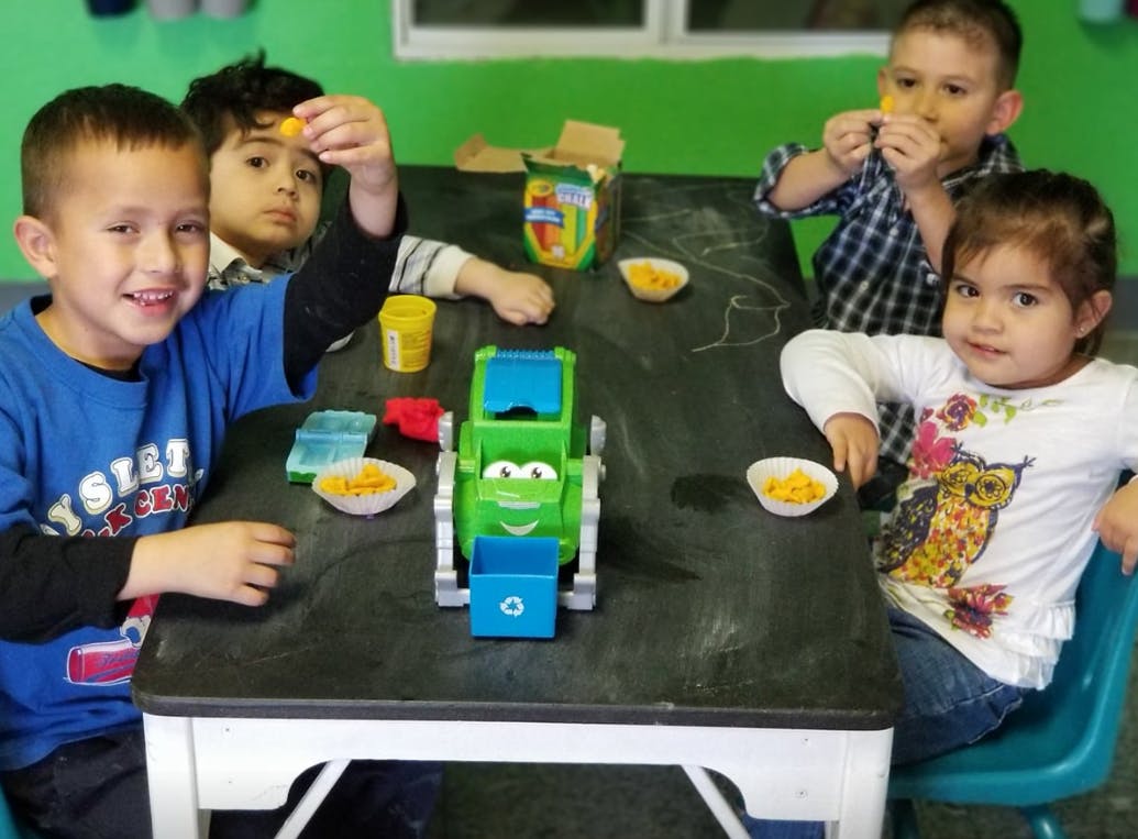 Children sitting at a table with snacks and a toy truck