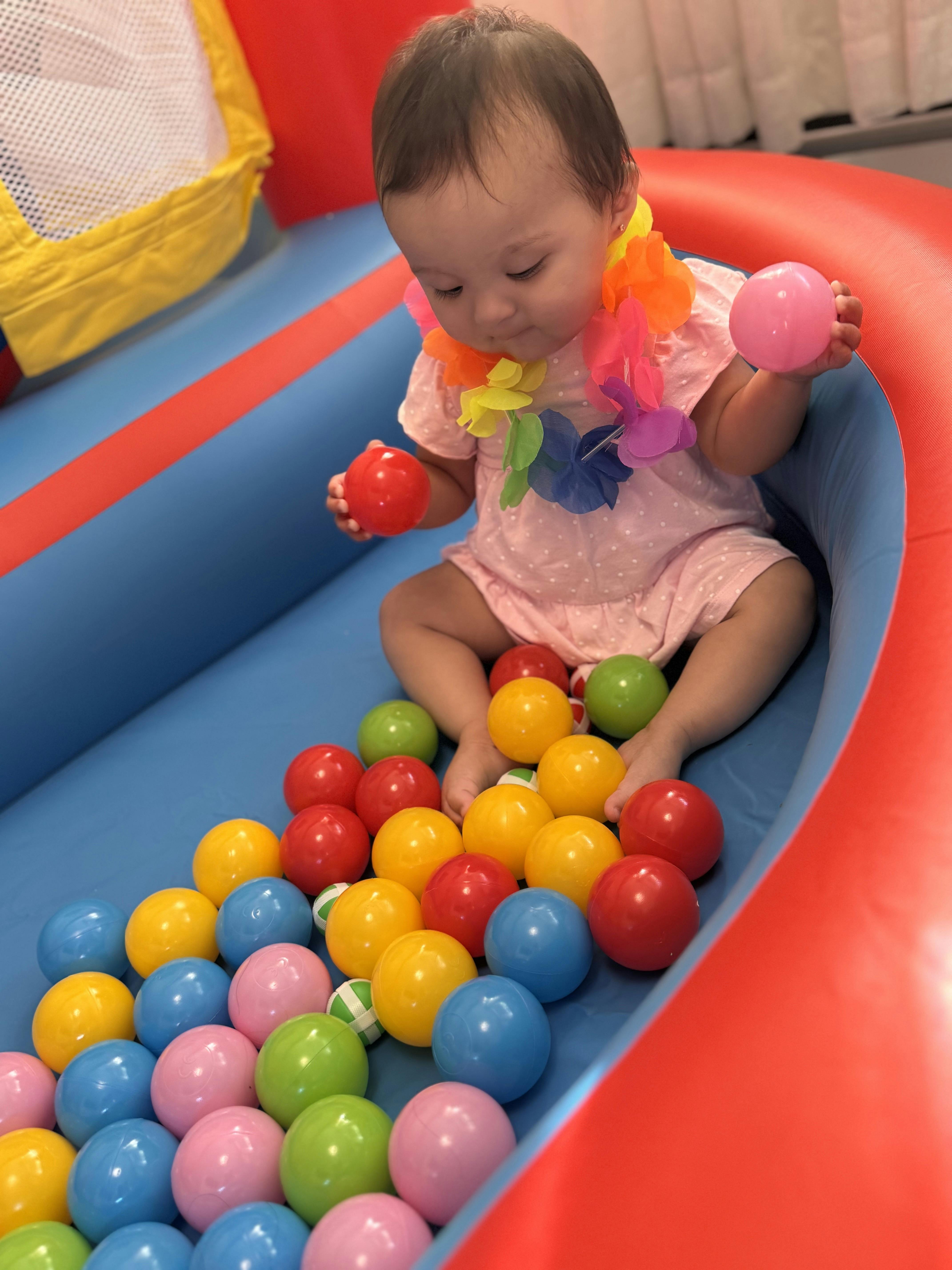 Child wearing a floral lei playing with colorful plastic balls in a ball pit
