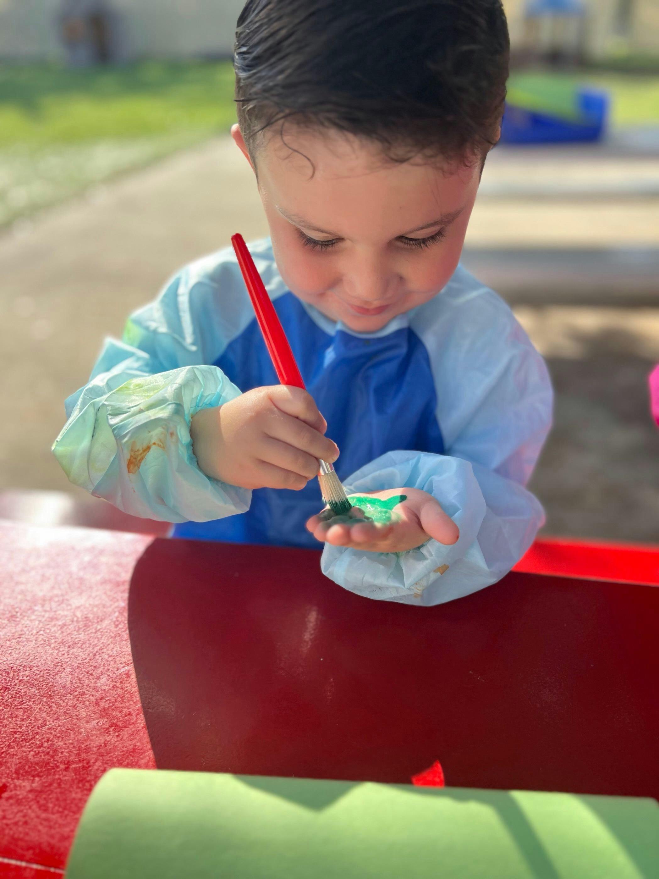 Child in smock painting green paint onto their hand