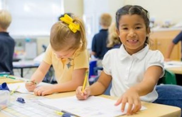 Two children writing at desks in a classroom