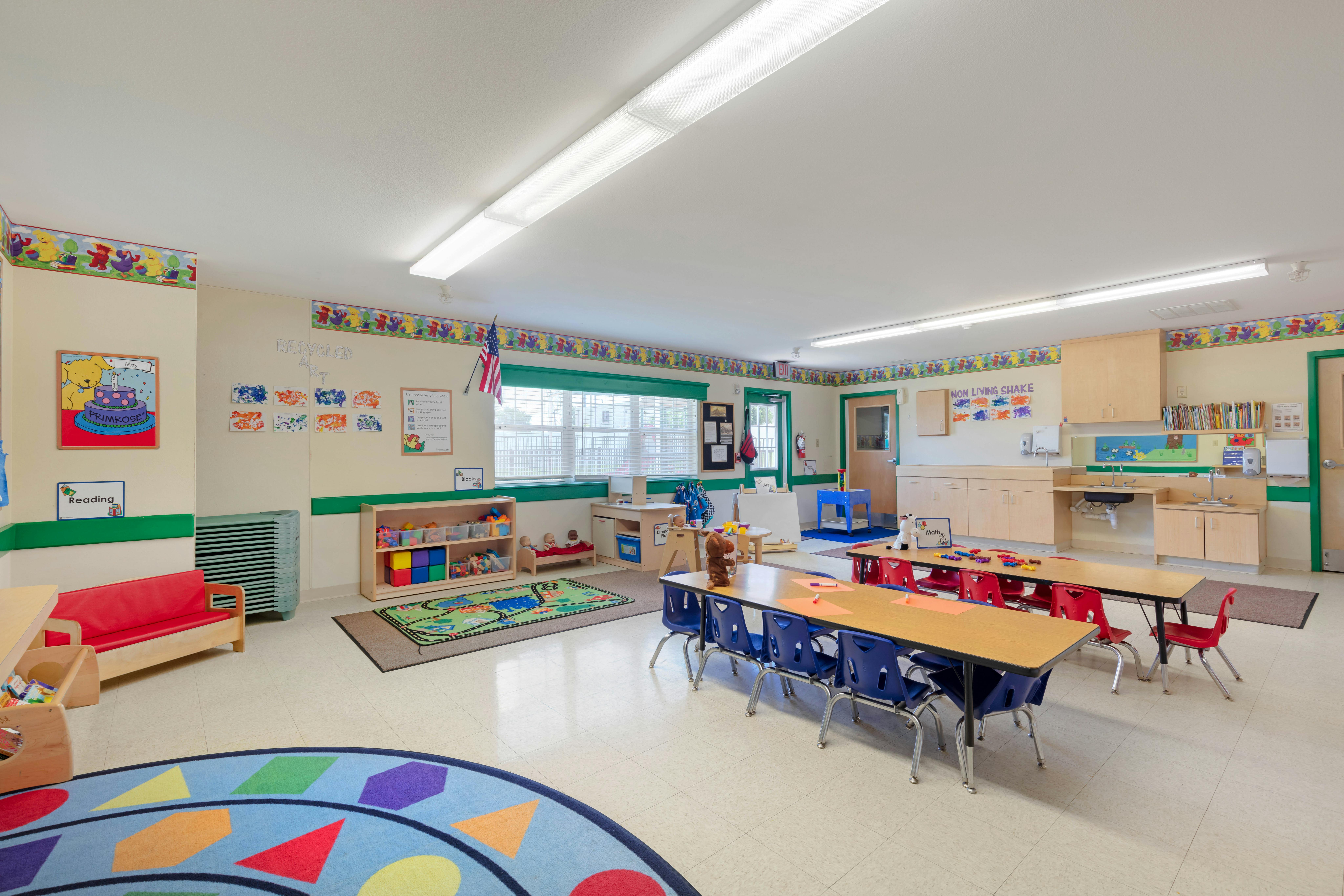 A classroom with tables and chairs, play mats, and learning materials