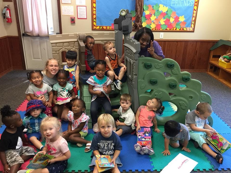 Adults and children sitting on and around a play structure in a classroom