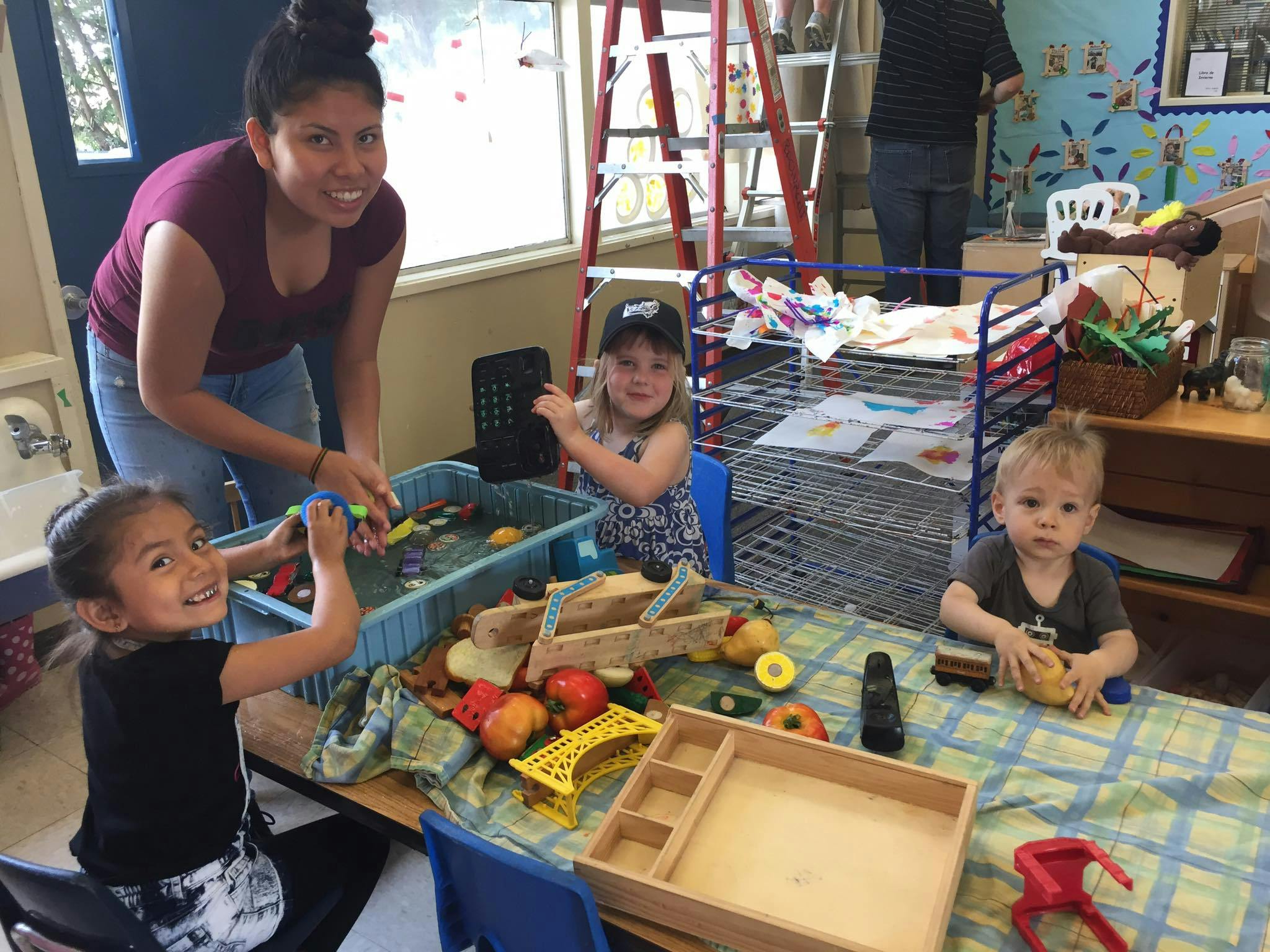 Adult and three children playing with toys and water in a classroom