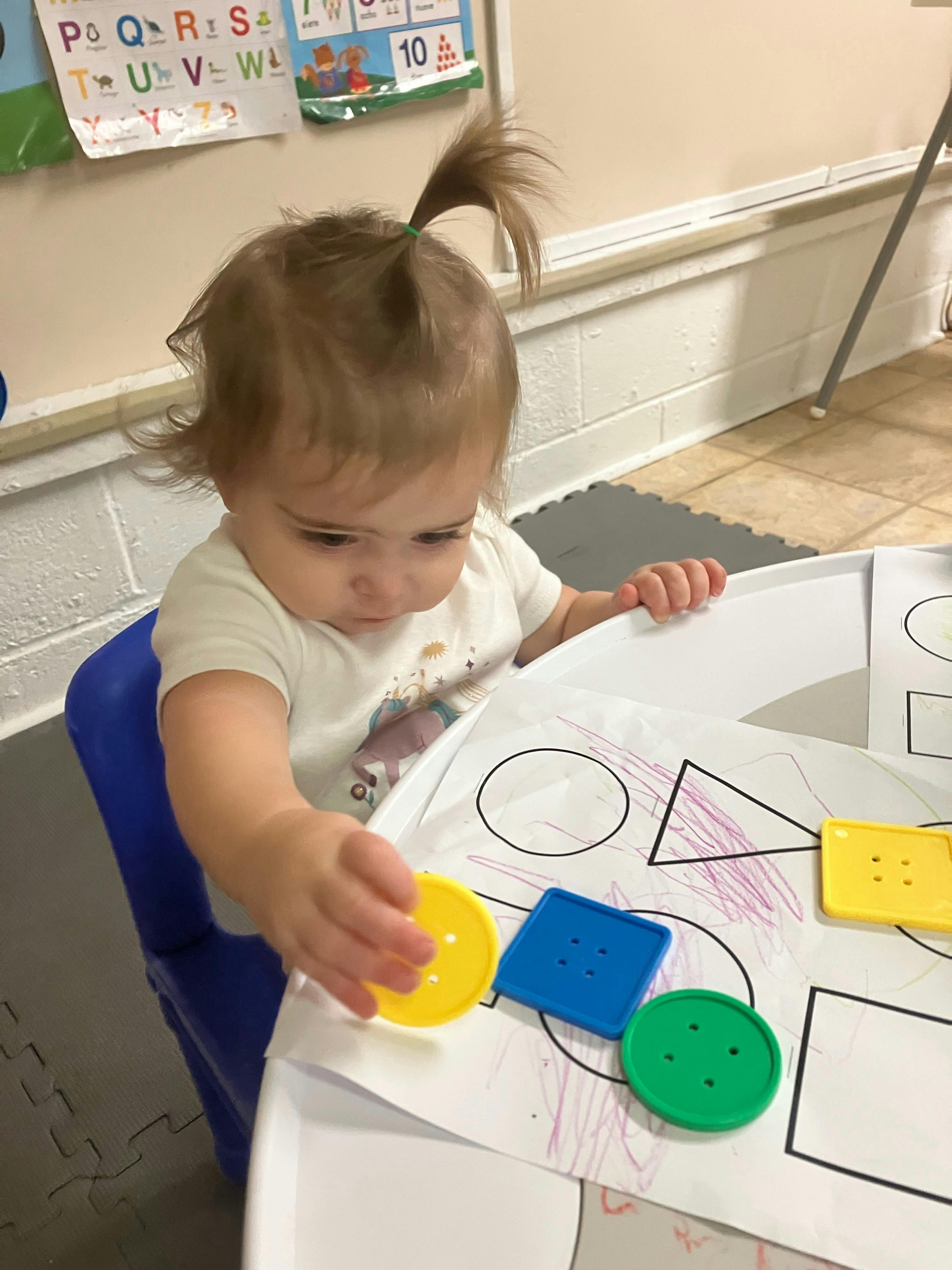 Child playing with colorful shape sorter pieces on a table