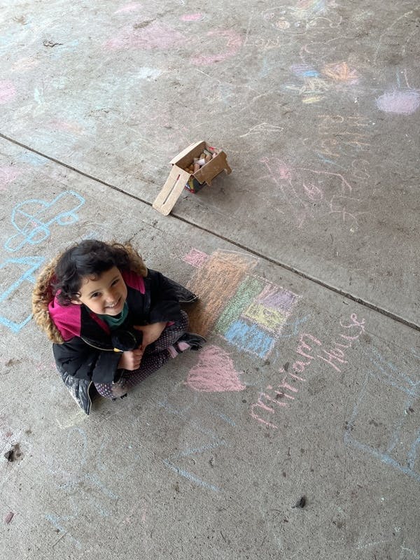 Child sitting on concrete next to chalk drawings