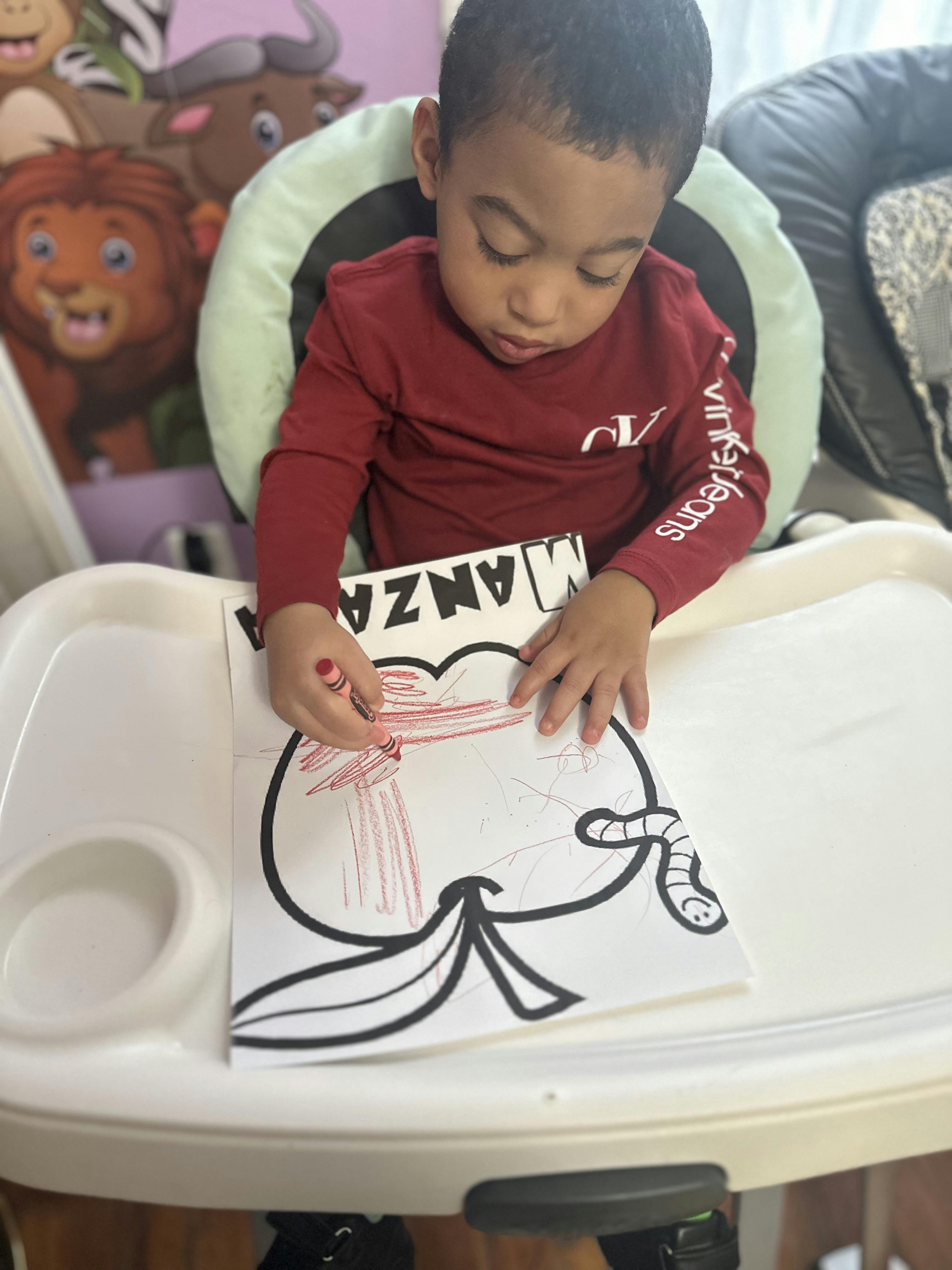 Child coloring a picture of an apple with a worm