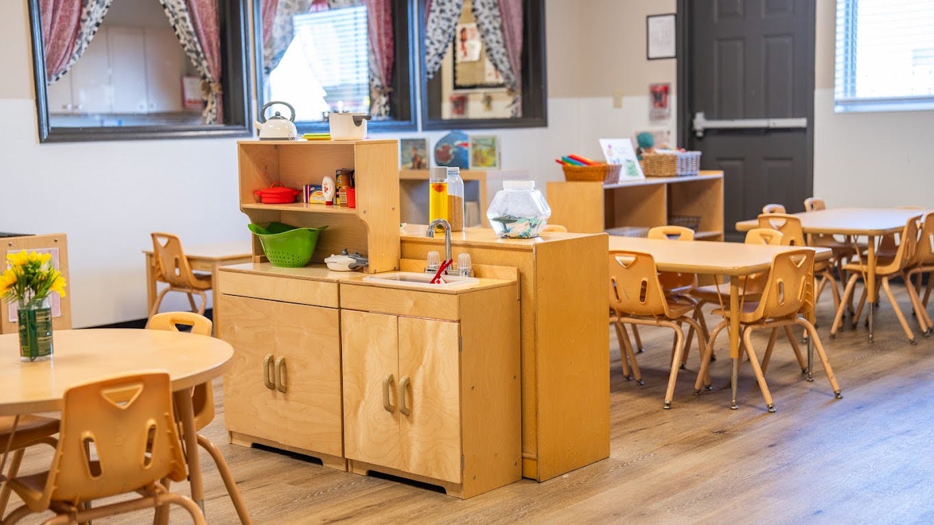 Wooden toy kitchen unit in a classroom with small chairs and tables