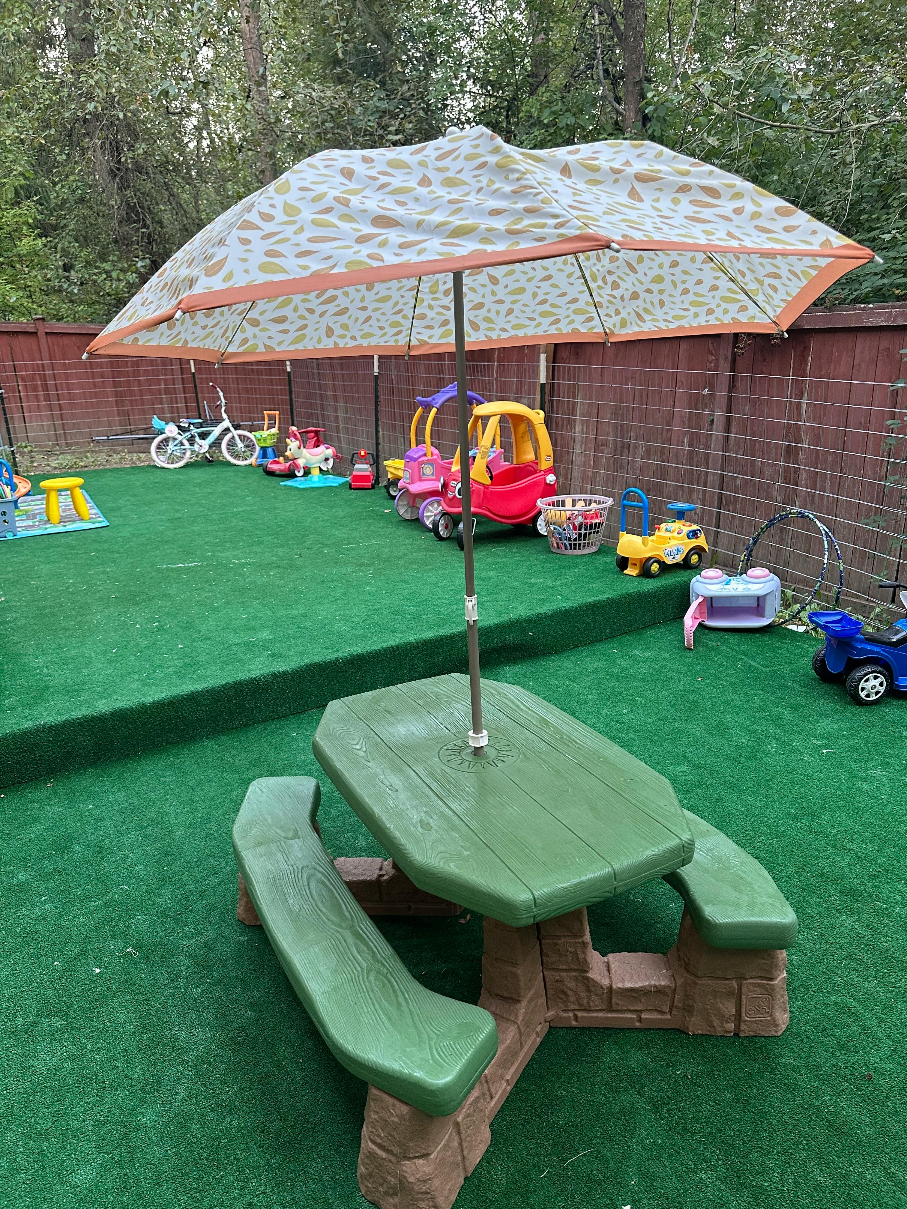 Outdoor play area with a picnic table, umbrella, and various toys