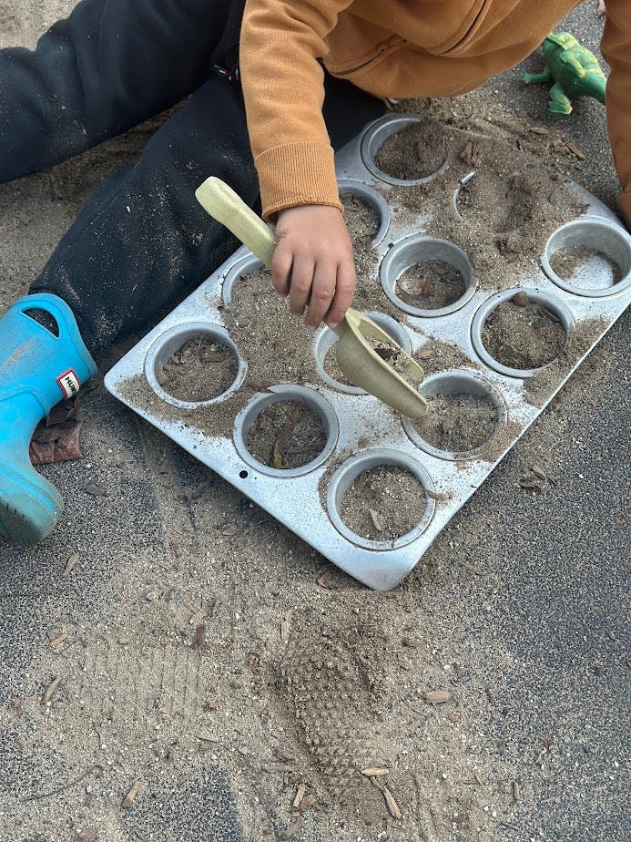 Child playing in sand with muffin tin and scoop
