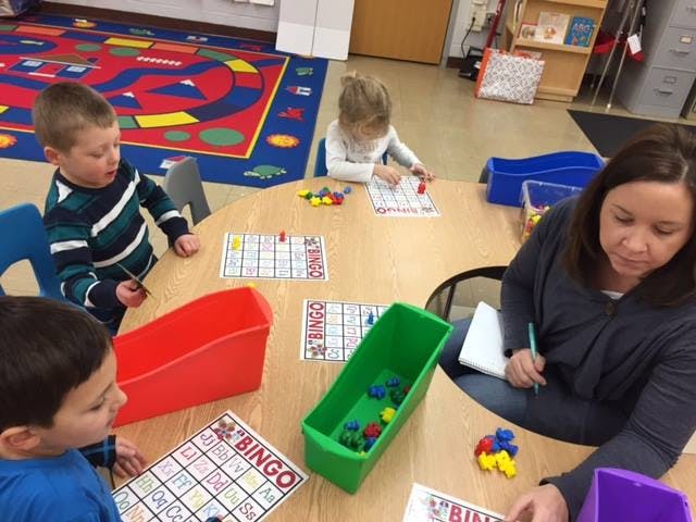 Adult and children playing bingo at a table in a classroom
