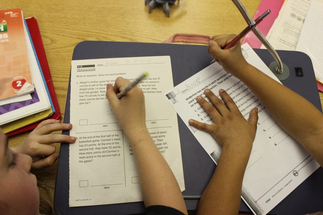 Two children writing on papers at a desk