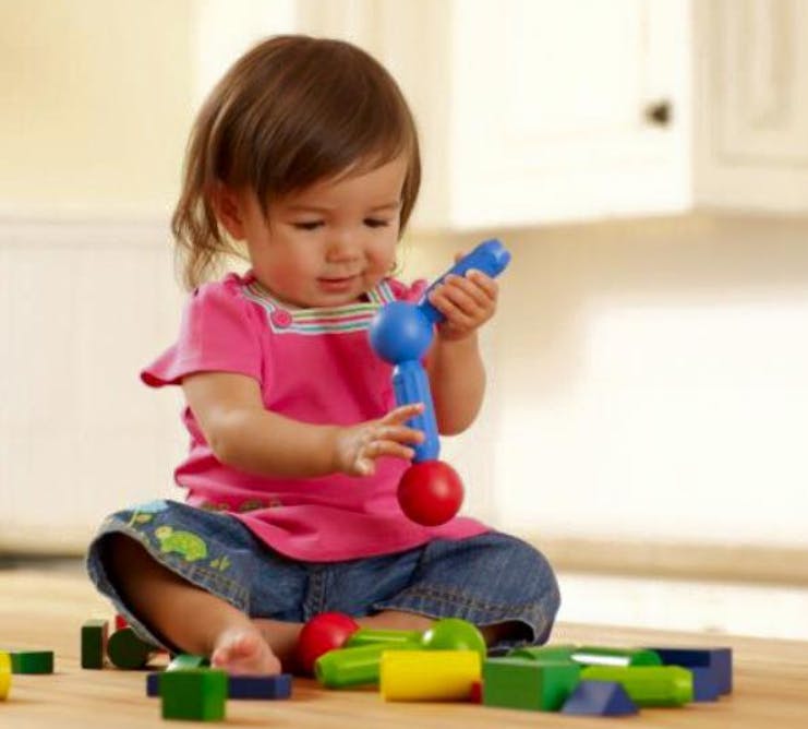 Child playing with a blue and red toy, with blocks on the floor