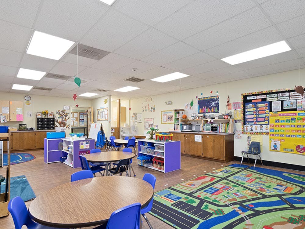 Empty classroom with small tables, chairs, and colorful play mats