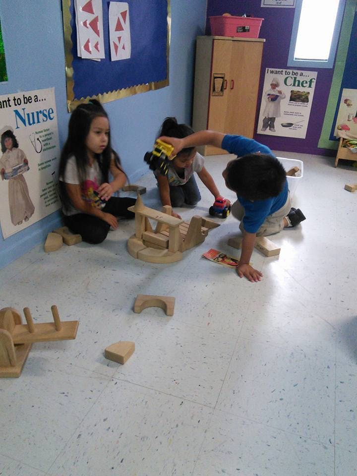 Three children playing with wooden blocks and toy cars on the floor