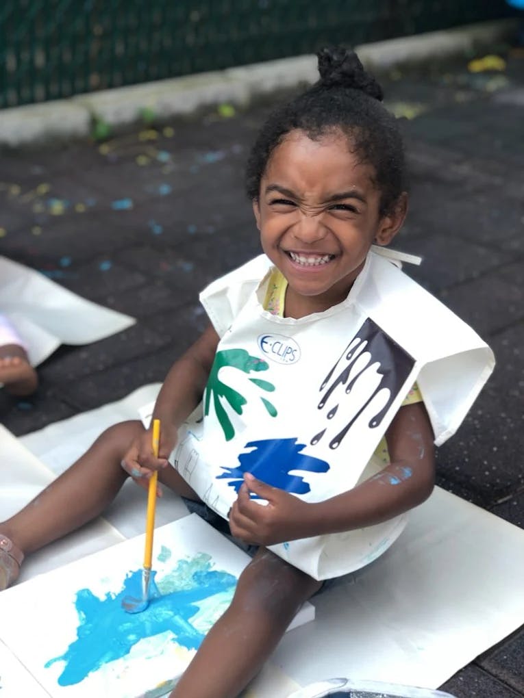 Child in a paint-splattered smock painting on paper