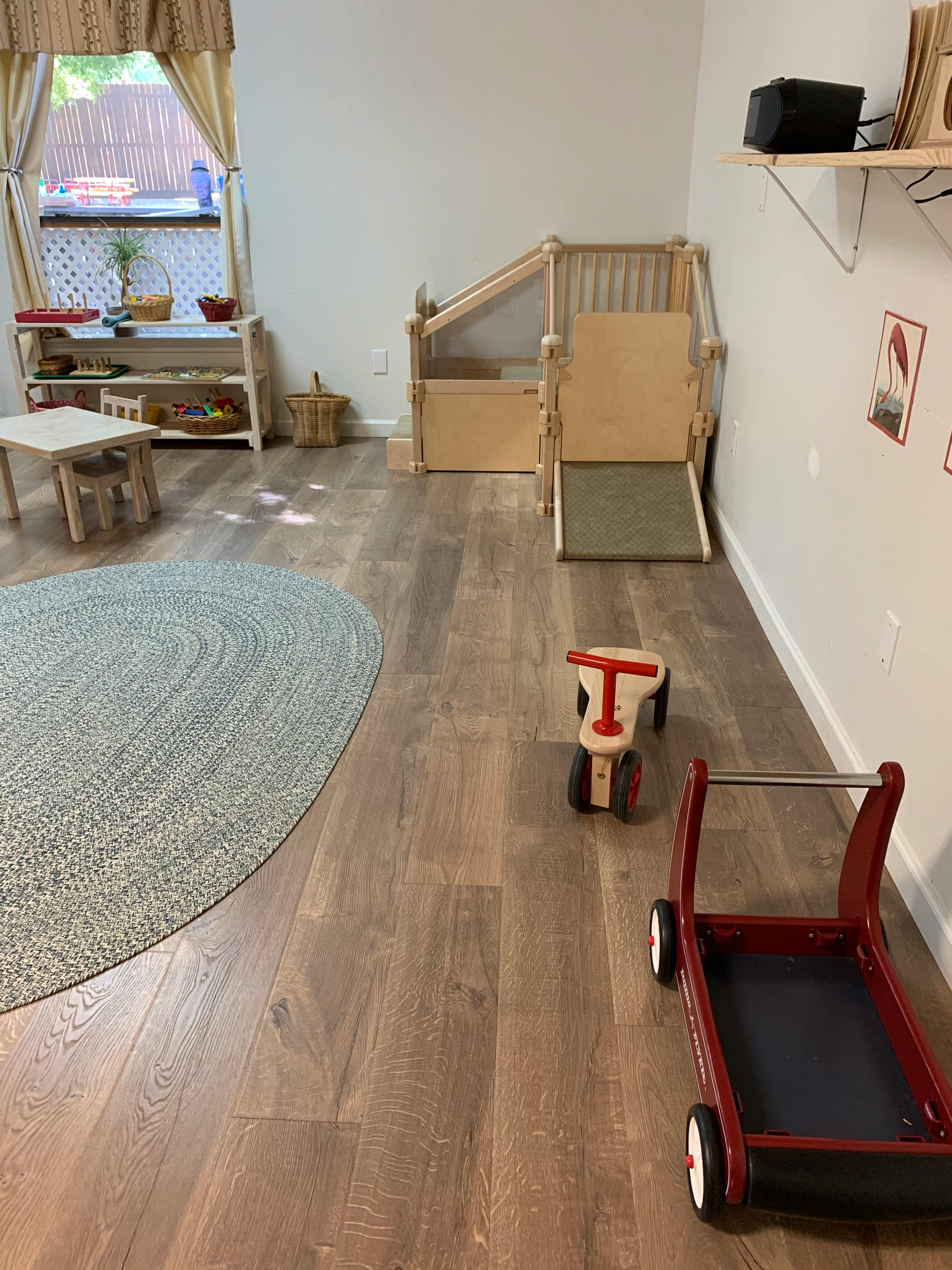 Playroom with wooden climbing structure, small table, and ride-on toys