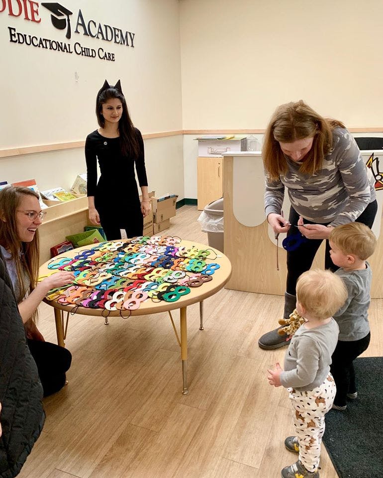 People and children around a table with colorful masks