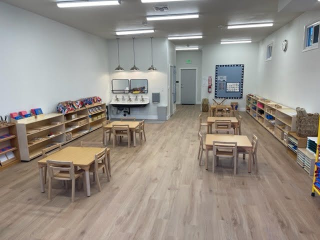 Empty classroom with small tables and chairs, shelves, and a sink area